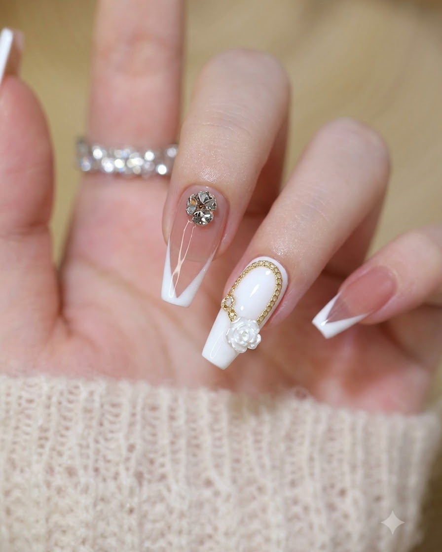 Primer plano de un juego terminado de uñas estilo hada con rosas blancas, cadenas doradas y cristales transparentes.