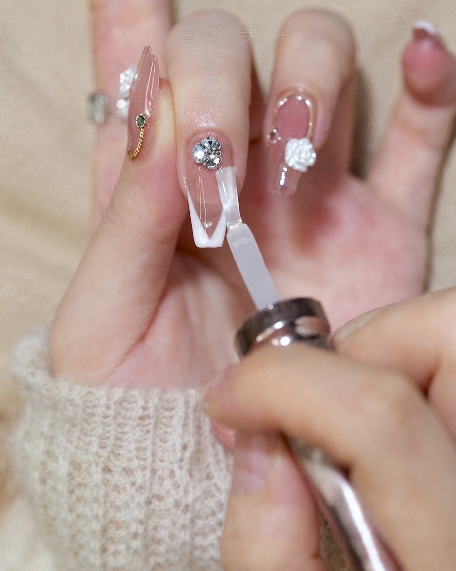 Un pincel de uñas aplicando una capa superior brillante en una uña con punta francesa mientras evita el grupo de cristales.
