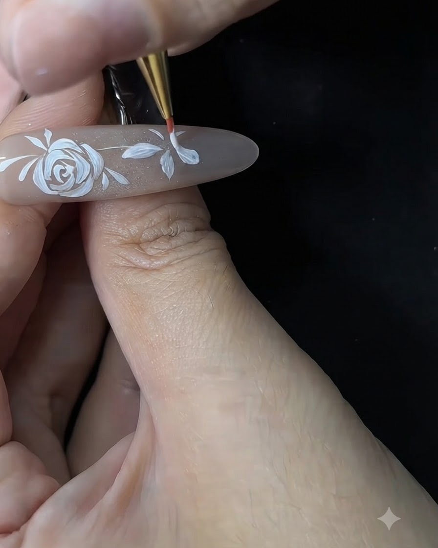 Una técnica de uñas usando un pincel fino para refinar y engrosar los pétalos blancos de una flor pequeña en una extensión de uña de gel.