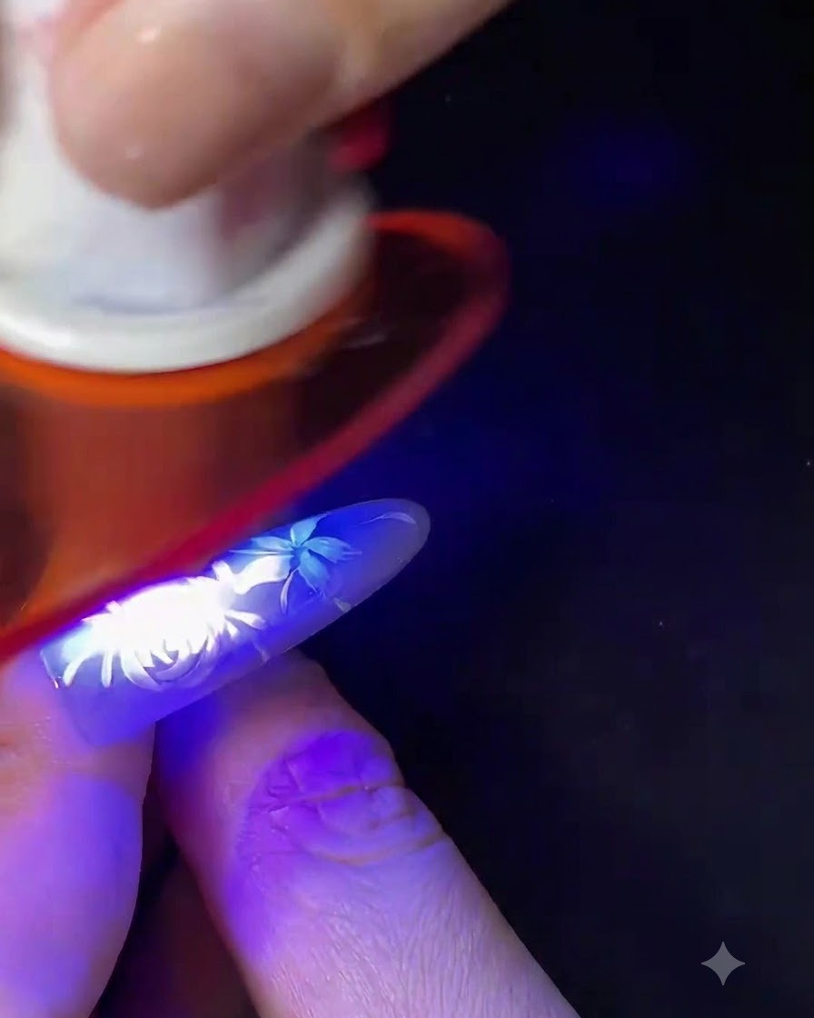 Un dedo con el nail art floral blanco completado curándose bajo una pequeña lámpara de uñas UV/LED azul.