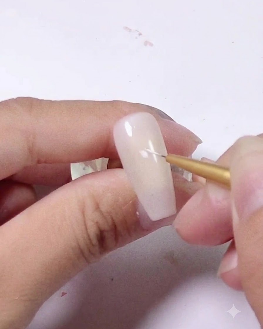 Un primer plano de un pincel delineador fino colocando un pequeño trazo blanco en una uña de color rosa claro.