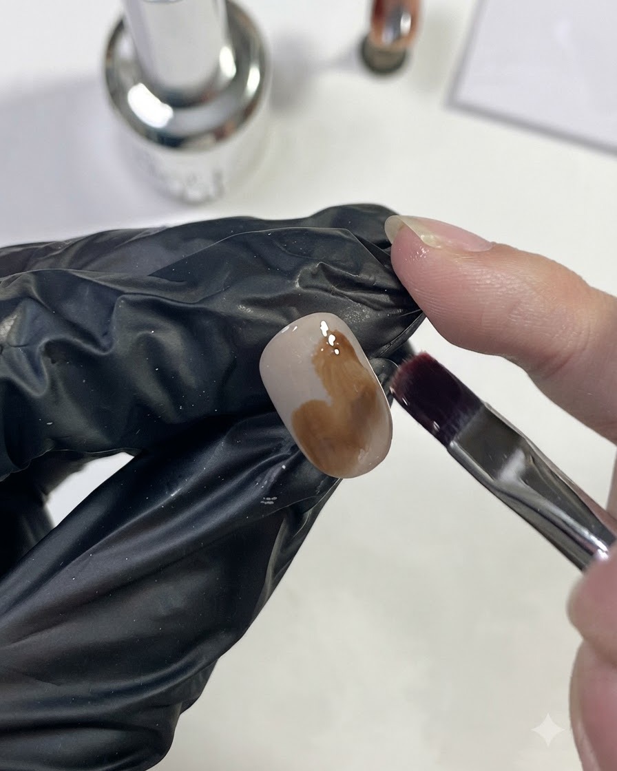 Un pincel de uñas aplicando gel marrón caramelo claro en una mancha grande sobre la uña.