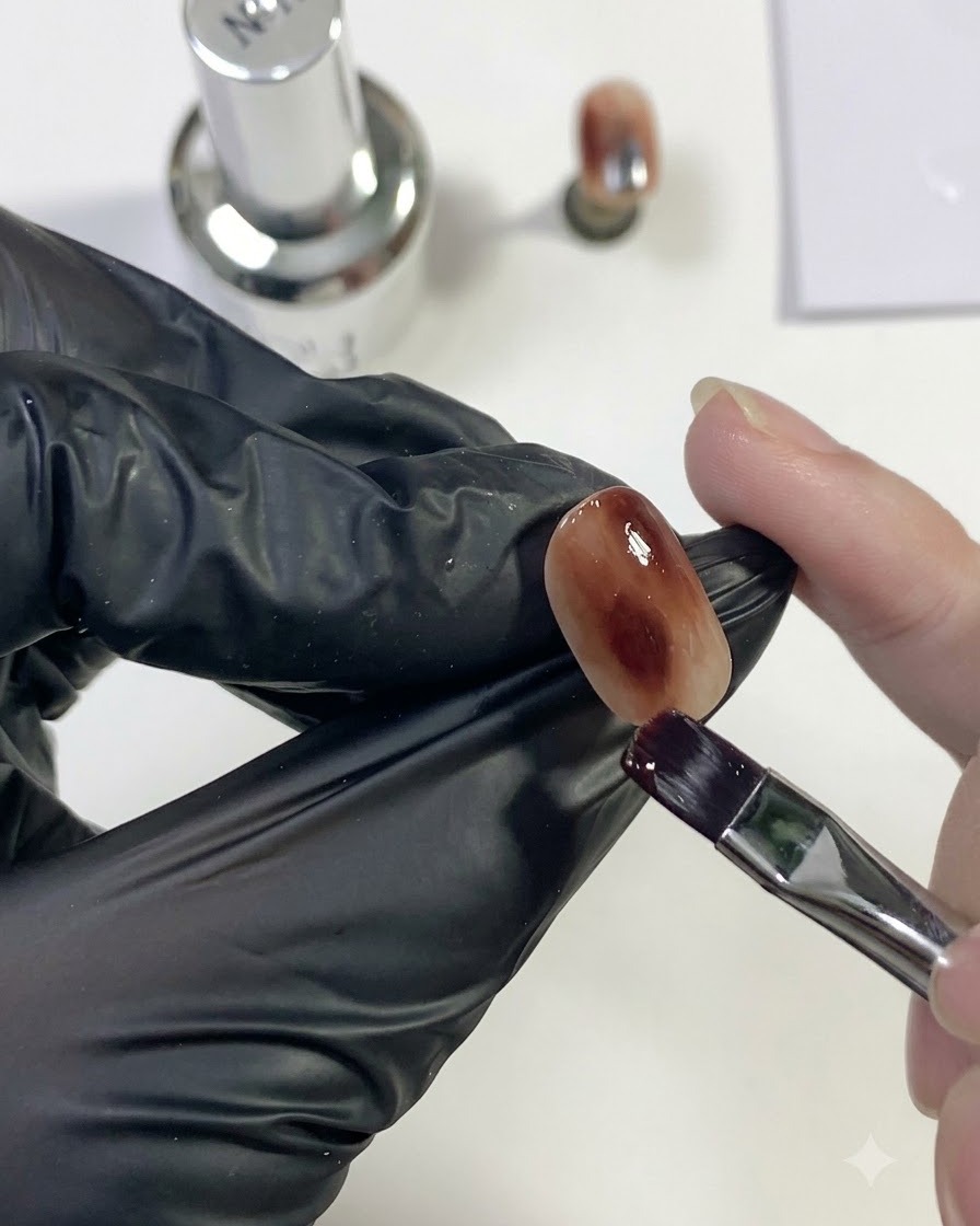 Un primer plano detallado que muestra un pincel desvaneciendo y mezclando suavemente gel marrón oscuro en el fondo ámbar.