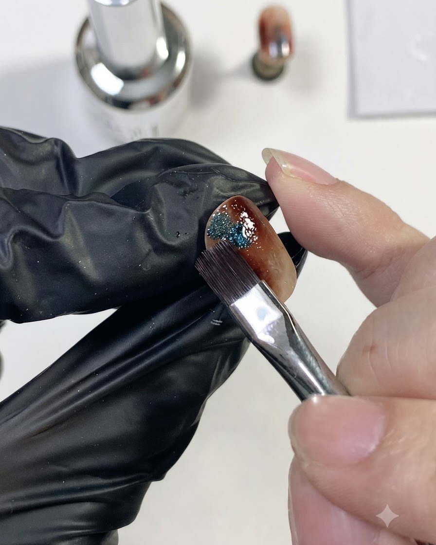 Un pincel de uñas colocando una pequeña gota de gel brillante ojo de gato magnético azul en el lateral de la uña ámbar.