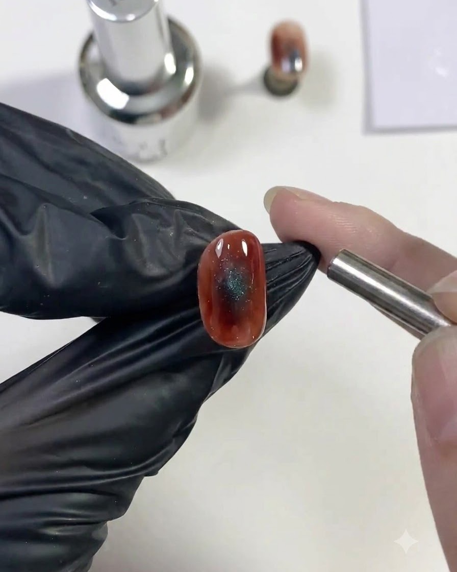 Un imán cilíndrico sostenido cerca de un diseño húmedo de uñas ojo de gato azul para atraer el reflejo de luz brillante.