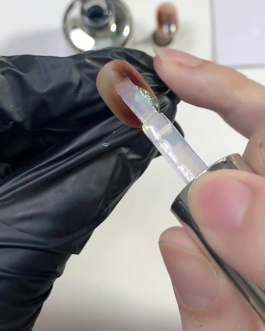 Un pincel deslizando una capa generosa de top coat transparente brillante sobre la uña ámbar con ojo de gato terminada.