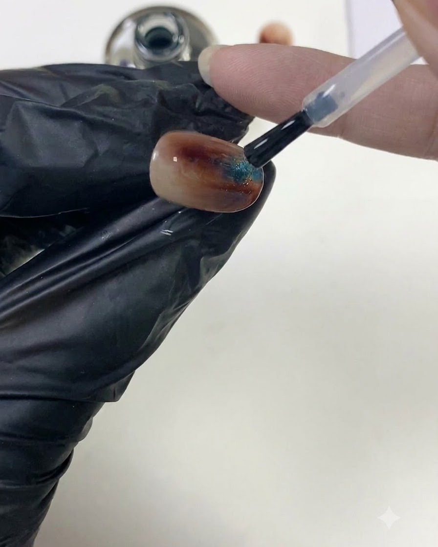 Un pincel de uñas alisando el top coat transparente sobre una superficie de uña ámbar texturizada para construir el ápice.