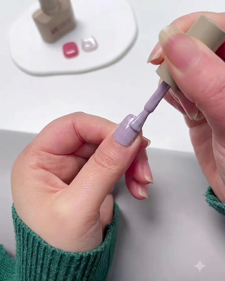 Un pincel de uñas aplicando esmalte en gel morado lavanda sobre una uña.