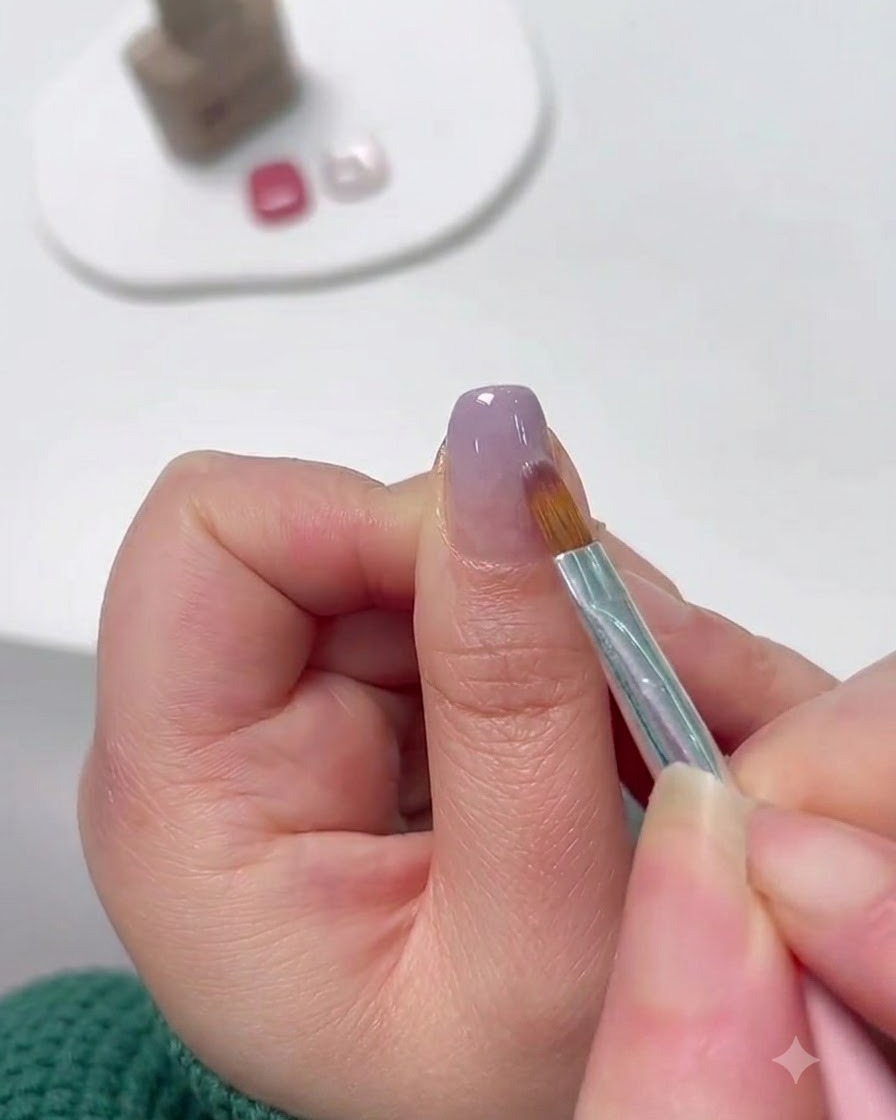 Un pincel de nail art detallado difuminando gel lavanda desde la punta hacia arriba para formar un degradado.