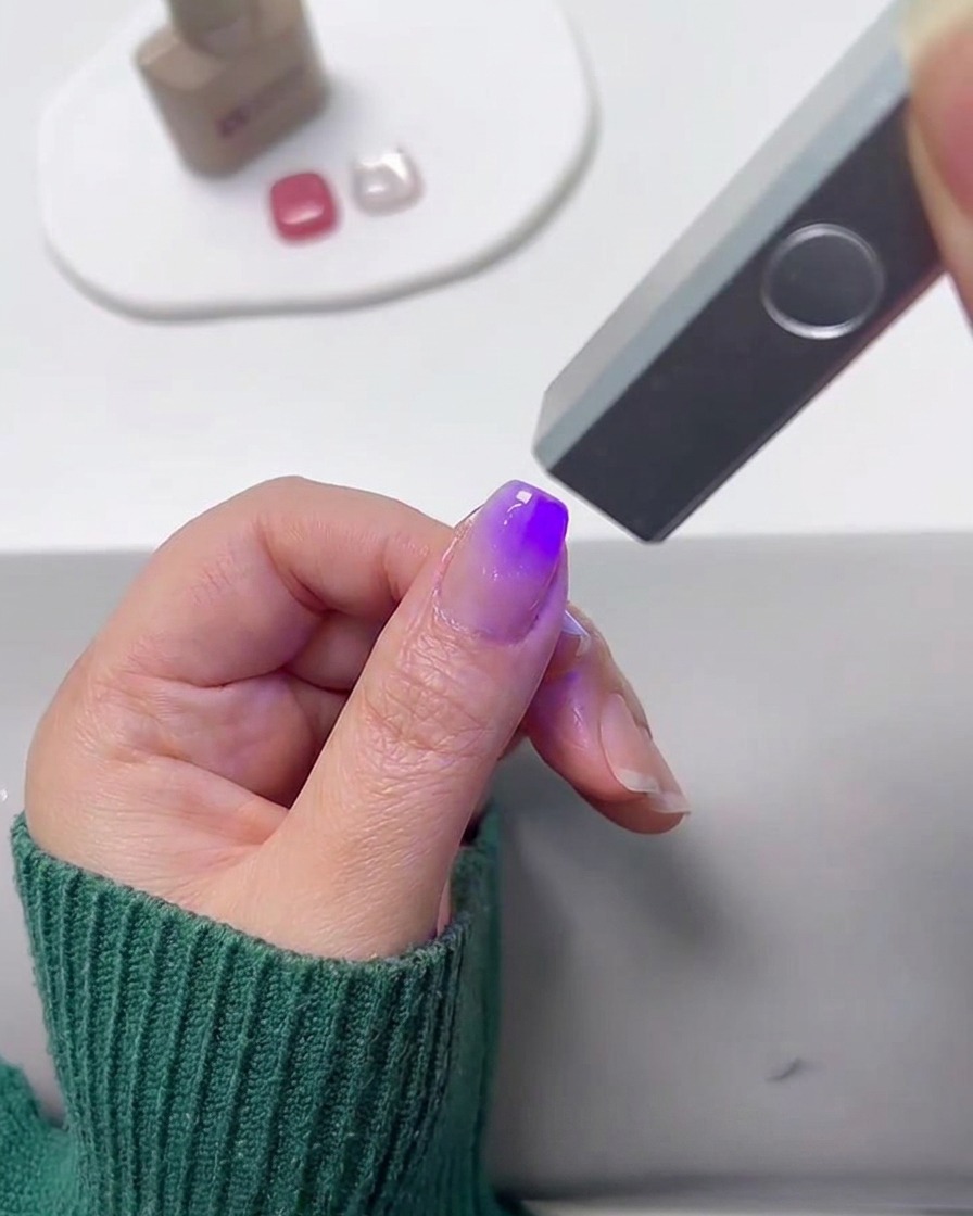 Una mini lámpara UV curando una uña pintada con degradado.