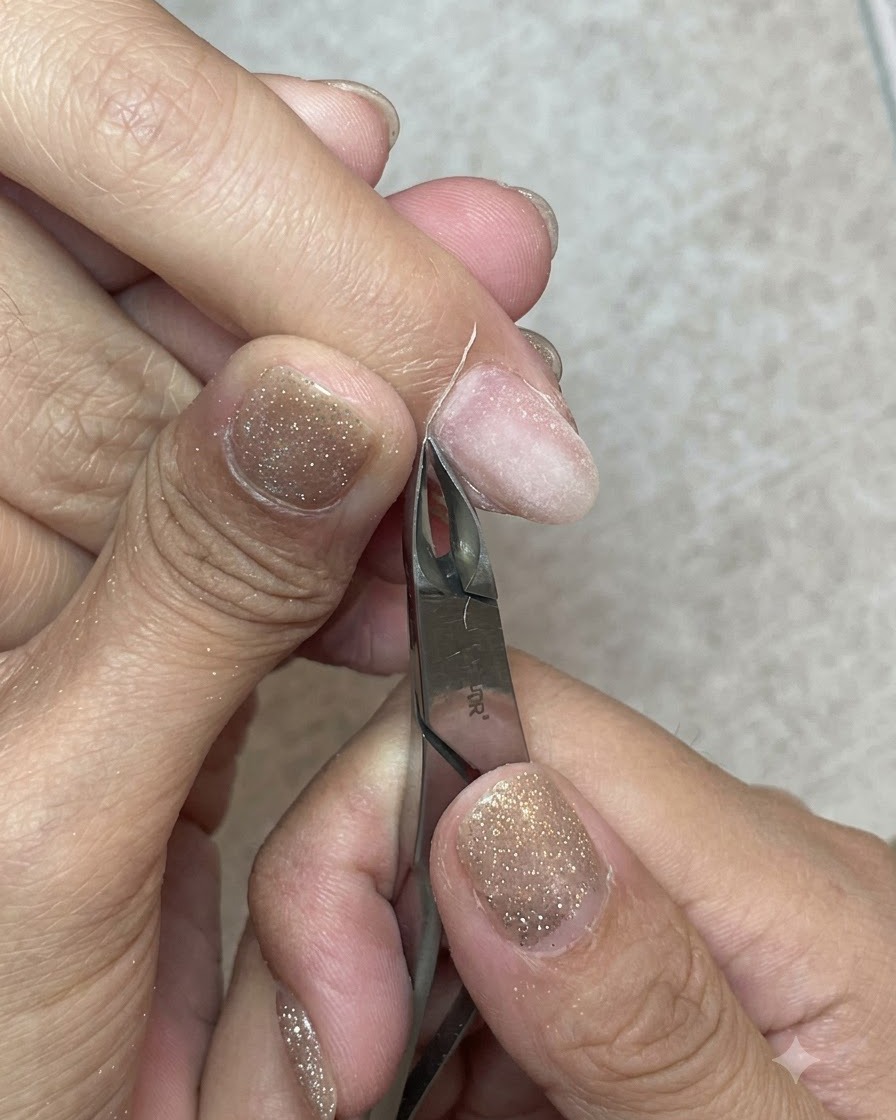 Unos alicates para cutículas de metal afilados cortando limpiamente una tira de piel muerta de la línea de la cutícula.