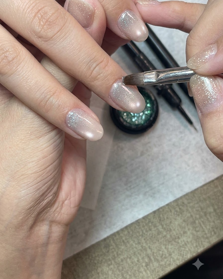 Un pincel de nail art detallado aplicando gel de purpurina de diamante triturado en la mitad inferior de una uña preparada.