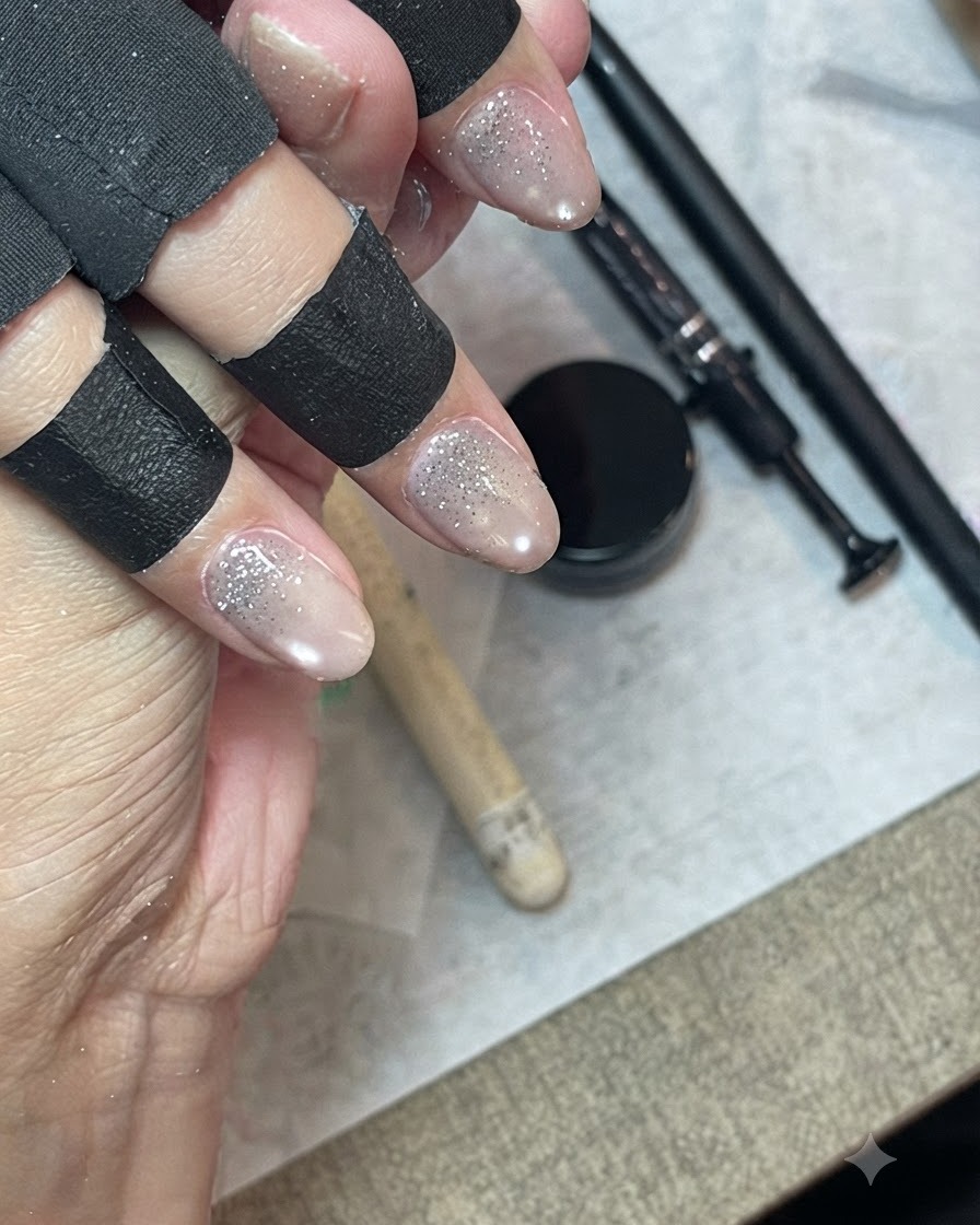 Una mano con protectores de dedos negros usando un pincel delineador fino para difuminar y extender el gel de purpurina a lo largo de la uña.