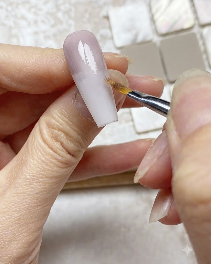 Un pincel ombré difuminando suavemente el borde de una capa de gel morado hacia abajo en una extensión de uña nude.