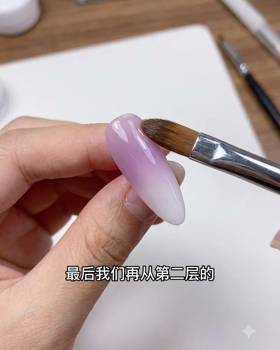 Un pincel de uñas limpio difuminando suavemente la línea de transición en una uña con degradado morado y blanco.