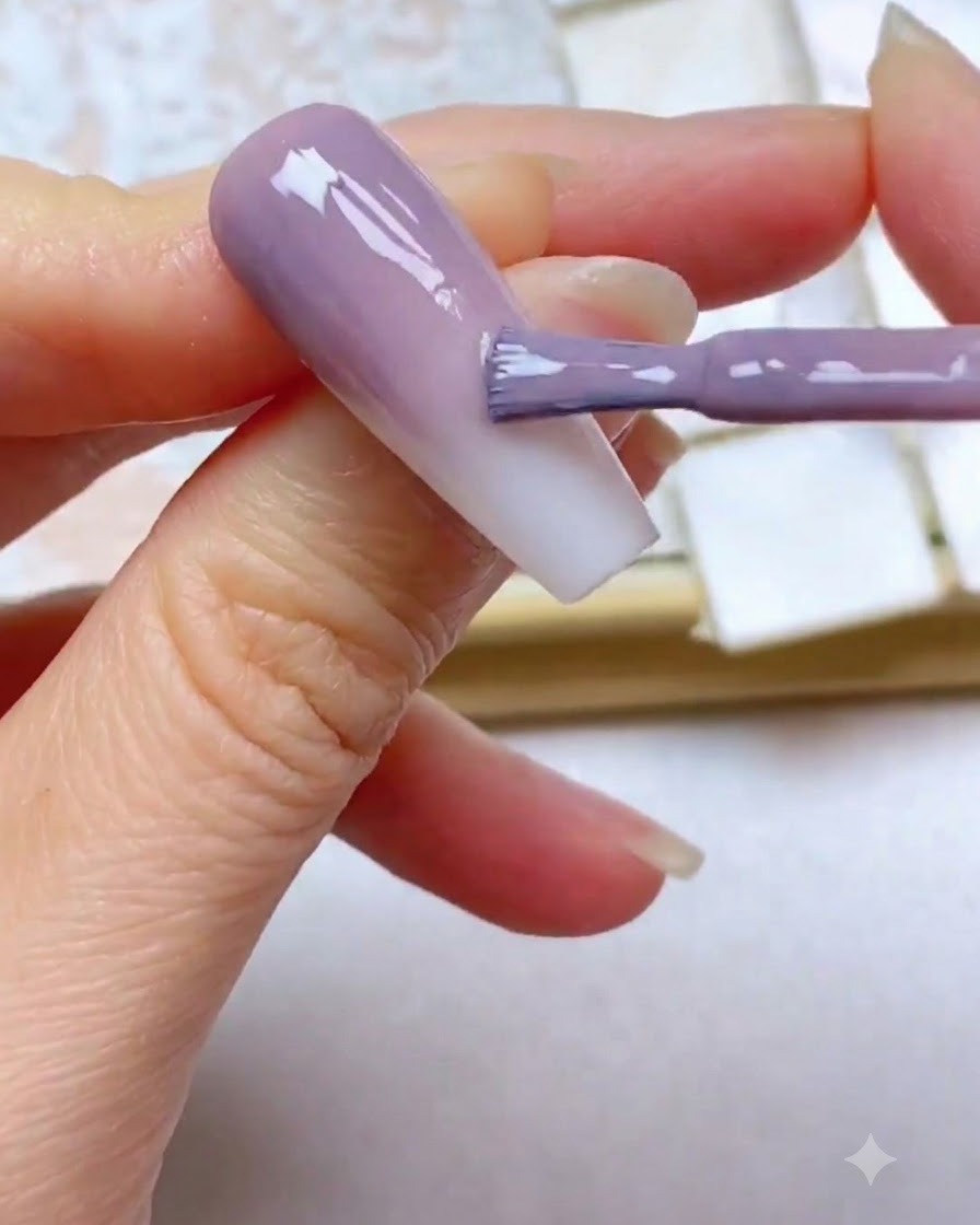 Un pincel de gel aplicando una tercera capa de color morado cerca del borde superior de la uña.