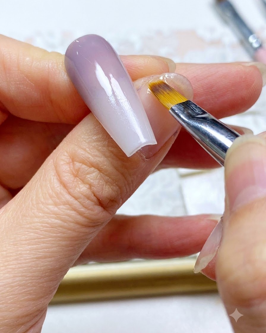 Un pincel de uñas haciendo un barrido de retoque final a lo largo de la sección de color difuminada de la uña.