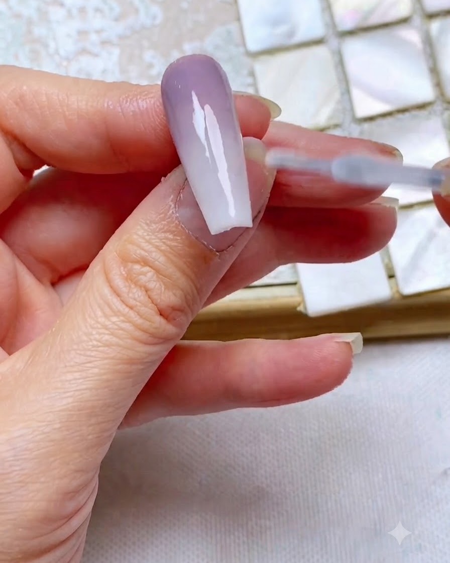Un pincel de top coat deslizándose suavemente sobre una uña con degradado bicolor terminada para sellar y aportar brillo.