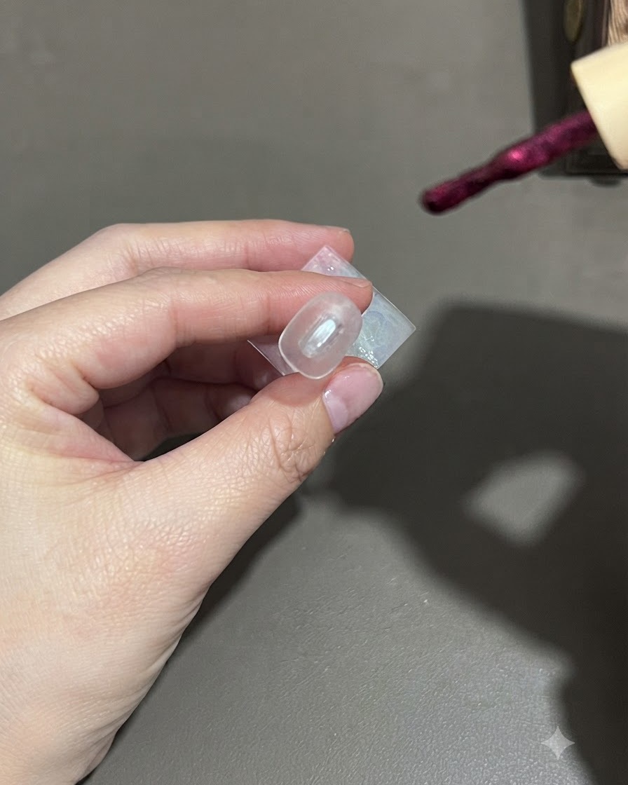 Un pincel aplicando esmalte de gel cat-eye morado oscuro sobre una uña.