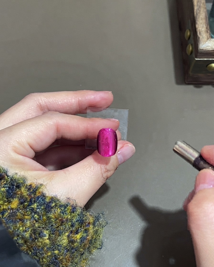 Un pequeño imán cilíndrico cerca de una uña de gel cat-eye rosa para dar forma al brillo.