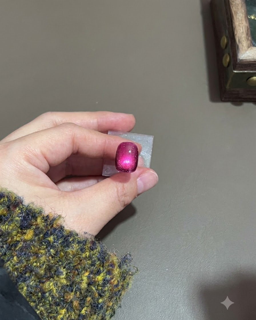 Una uña cat-eye morado oscuro con un brillo luminoso curado bajo una lámpara.