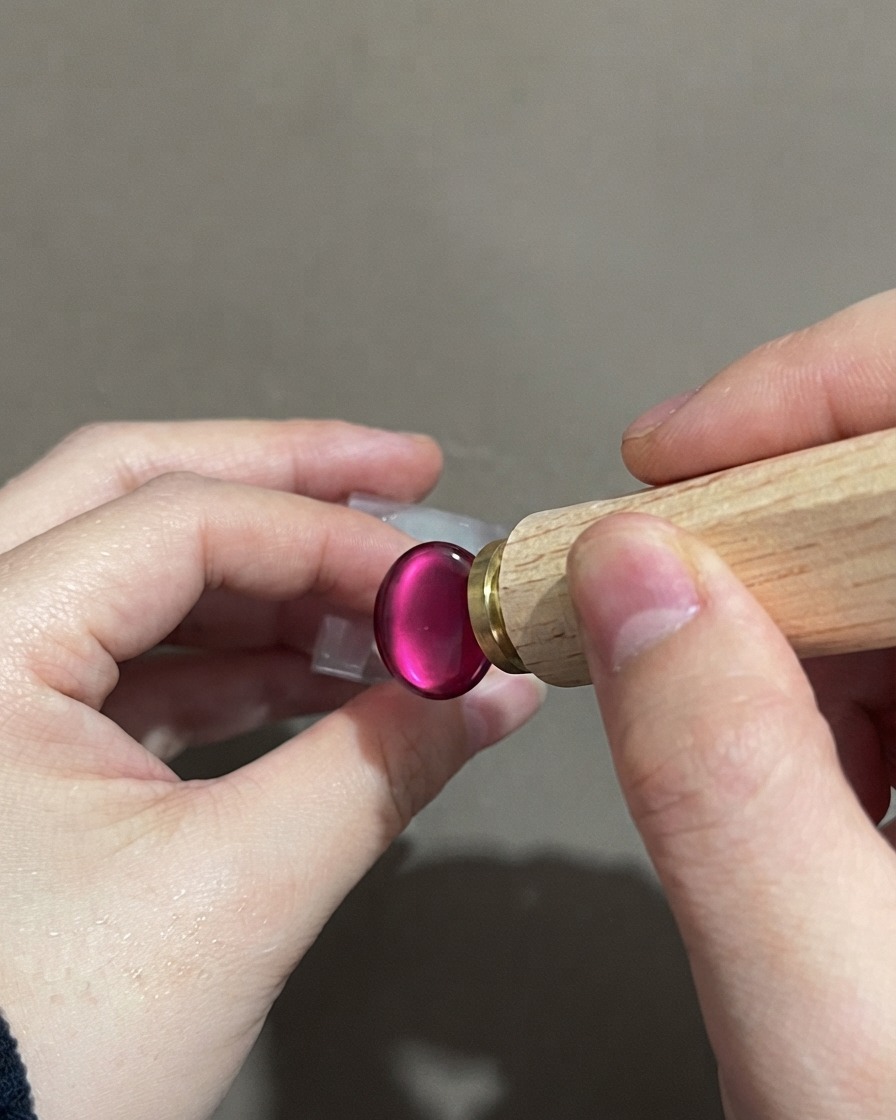 Una mano sosteniendo una herramienta de estampado de uñas cerca de una uña cat-eye degradada morada terminada.