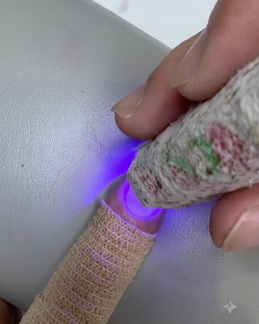 Una mini lámpara UV LED con patrones sostenida sobre la punta de una uña, curando una capa difuminada de gel transparente.