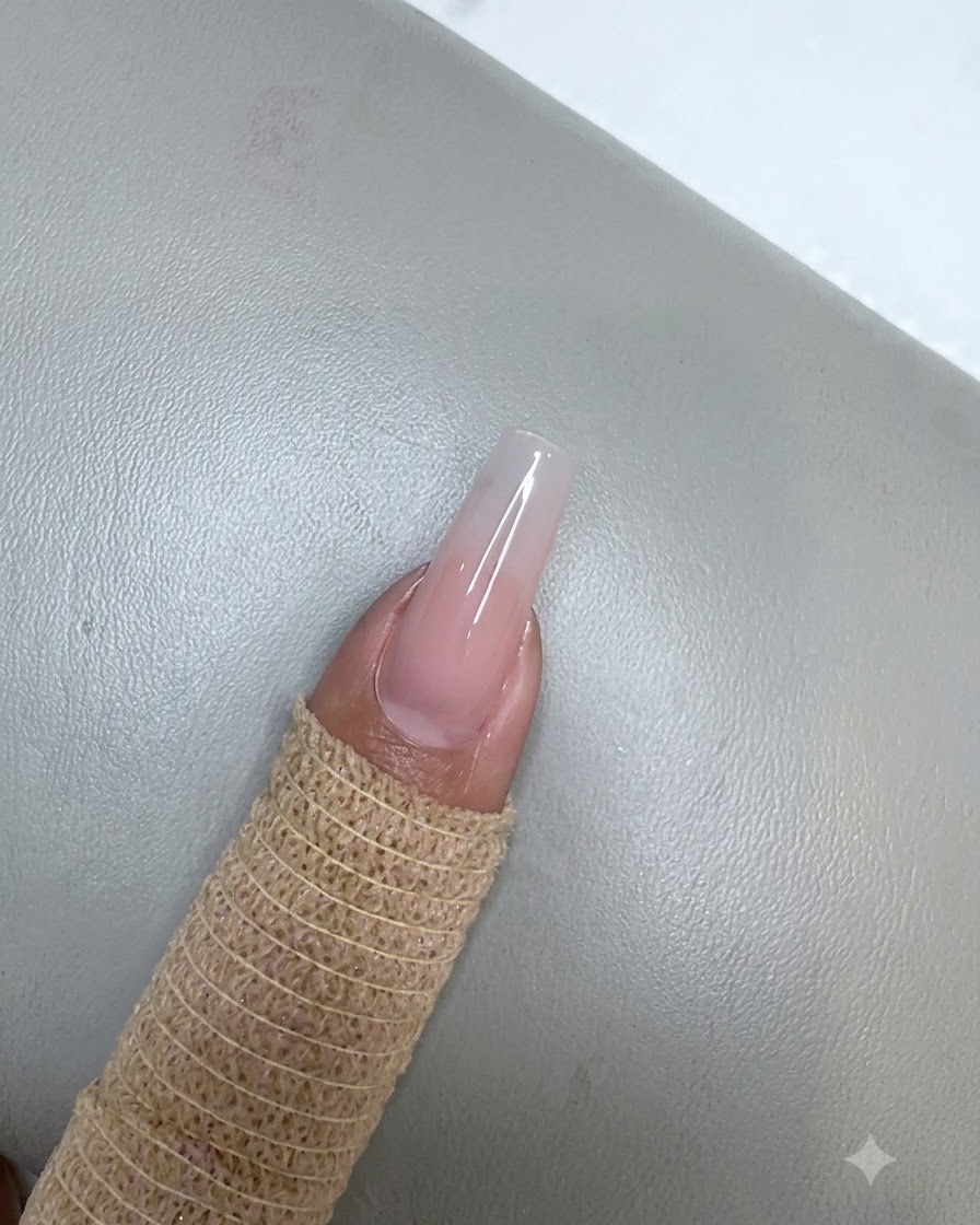 Una uña con una aplicación de gel rosa nude curada que descansa debajo de una pequeña lámpara UV LED púrpura.