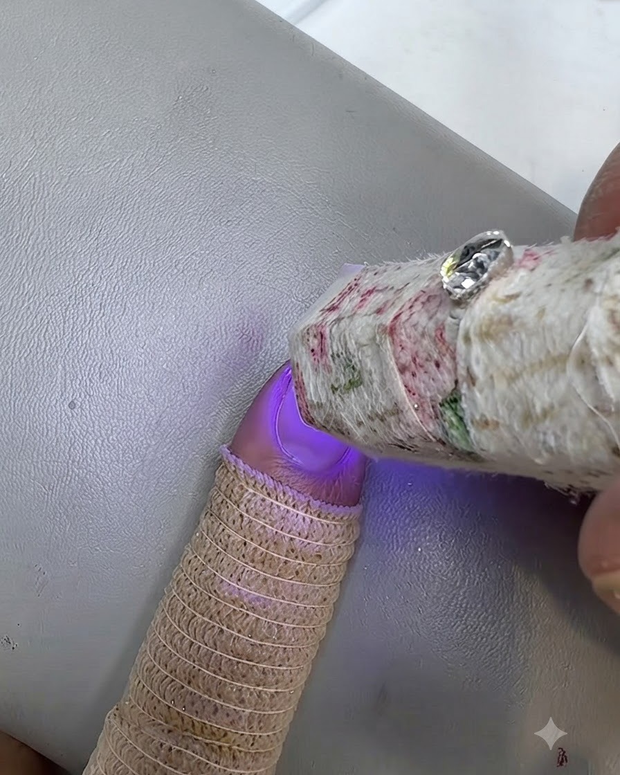 Una pequeña lámpara UV curando una uña pintada con un dedo que lleva un protector de punto.
