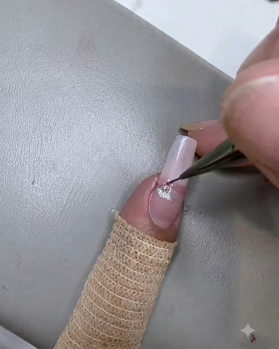 Un pincel delineador fino aplicando una segunda raya de gel cat eye rosa debajo de la raya plateada en la uña.