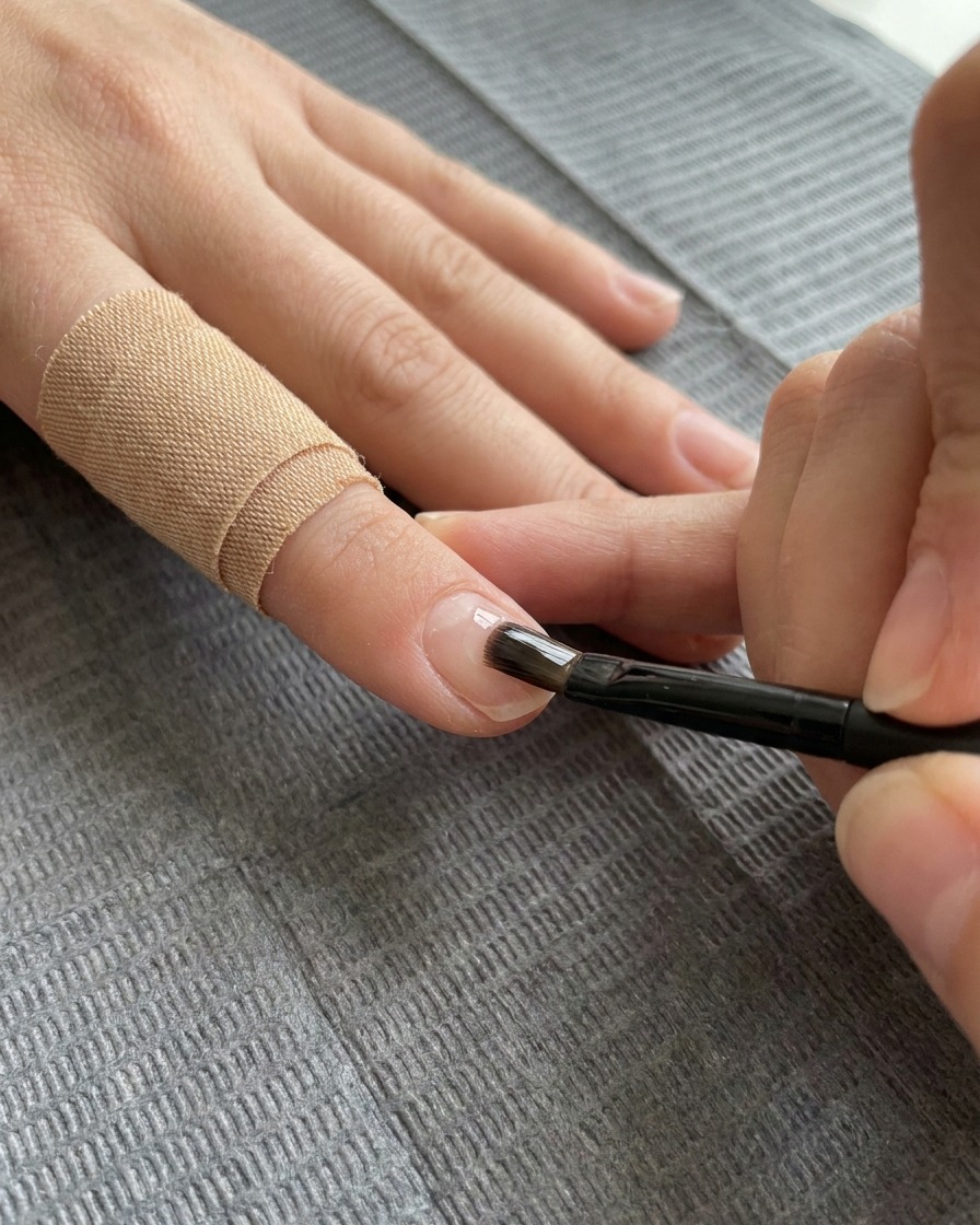 Un pincel de gel plano aplicando una capa transparente de gel de refuerzo sobre la uña decorada.