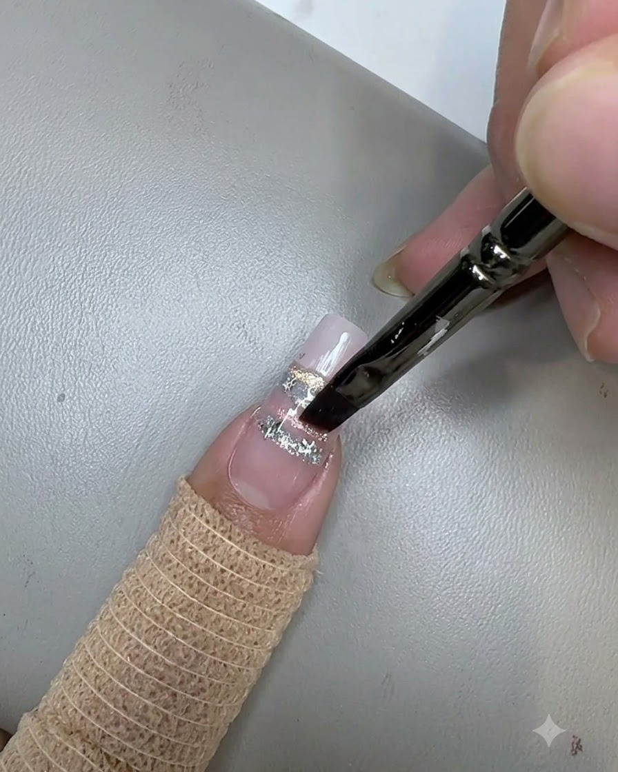 Un pincel de uñas aplicando un top coat transparente sobre las lentejuelas de estrellas en una uña decorada.