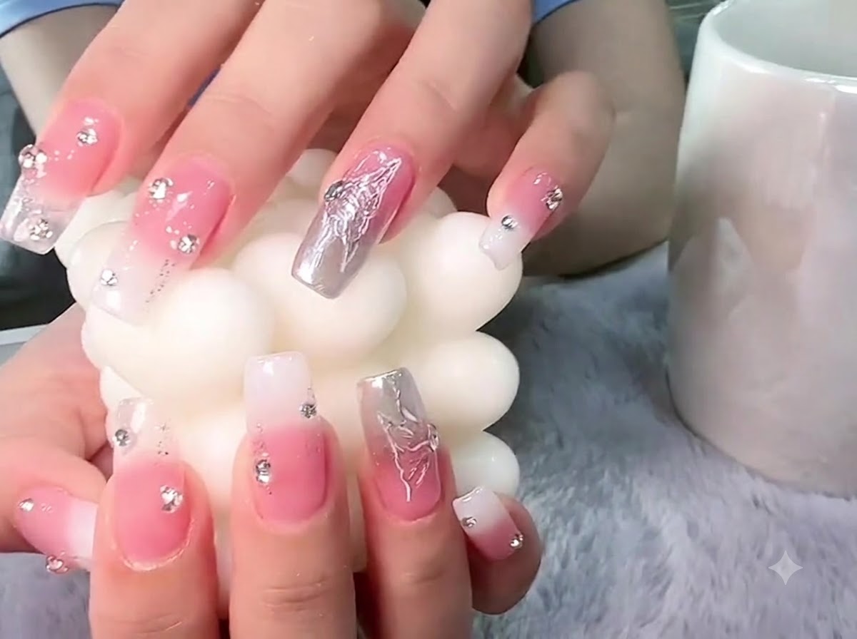 Manos sosteniendo un pilar de vela blanco texturizado con enfoque en el arte de uñas de mariposa plateada en 3D.