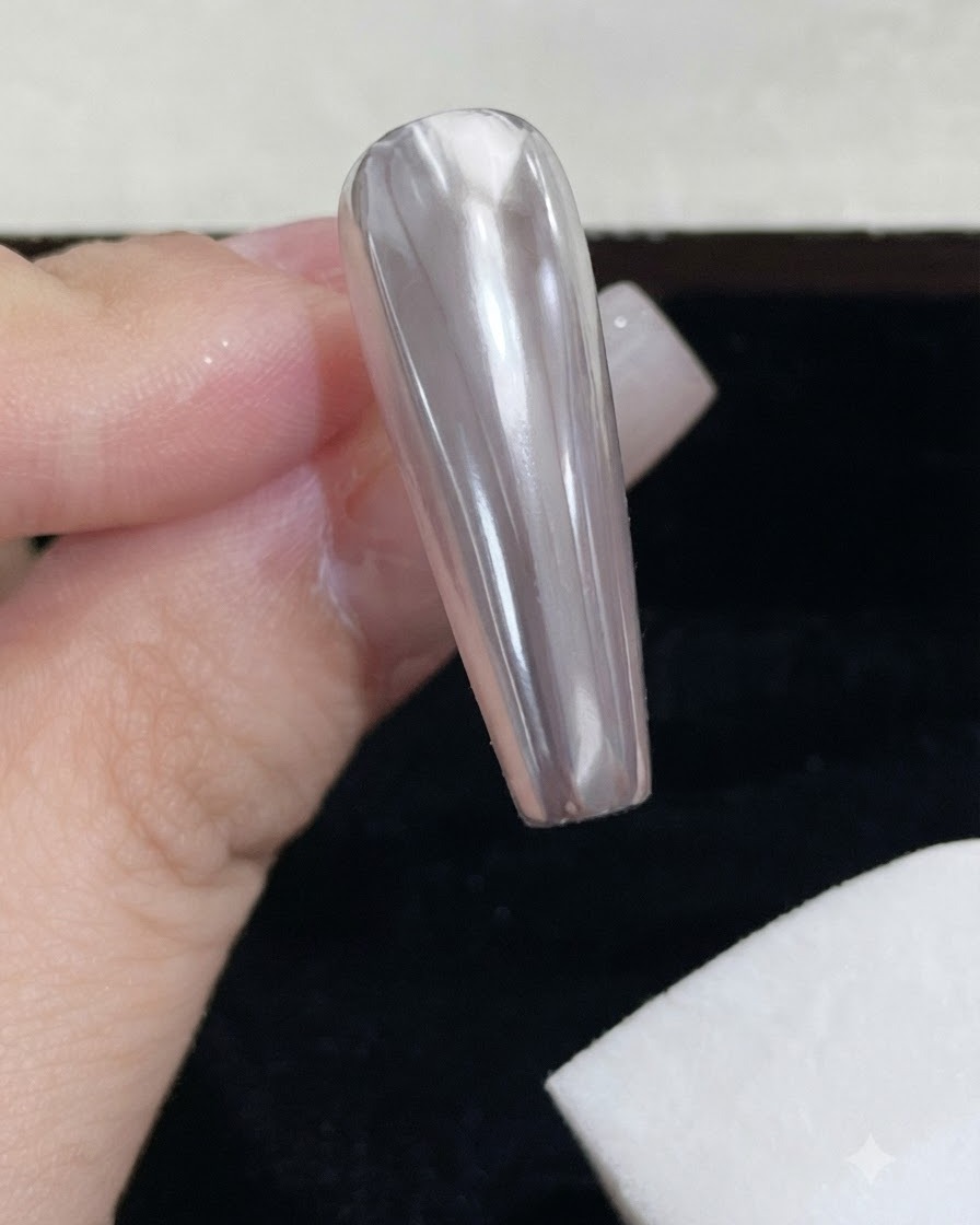Un bloque de esponja de espuma blanca limpiando el exceso de polvo espejo suelto de una uña cromada brillante.