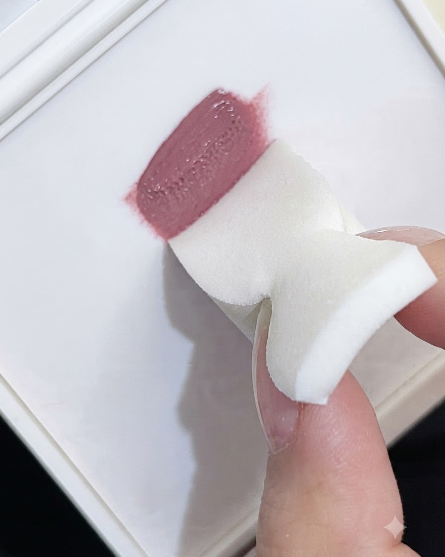 El borde de una esponja de espuma blanca recogiendo gel de color malva de una paleta.