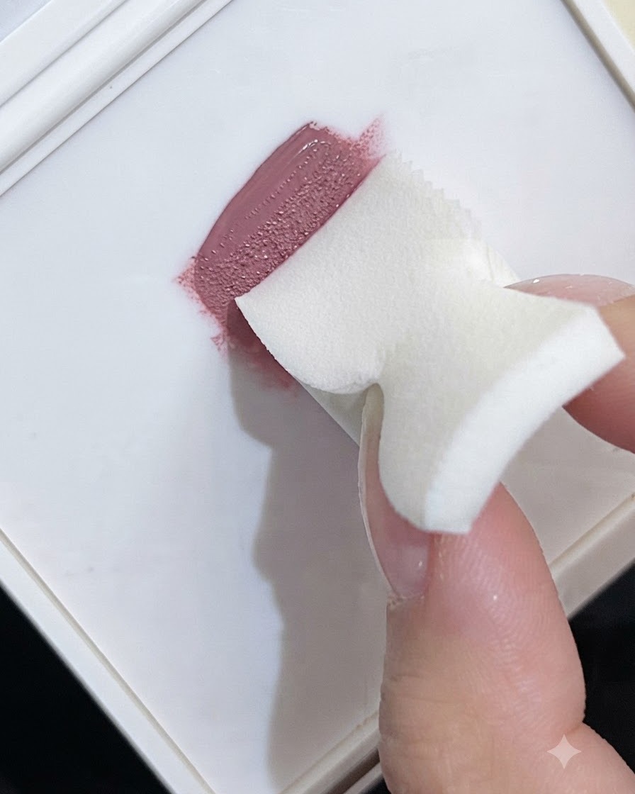 Una esponja de maquillaje de espuma recogiendo esmalte en gel rosa de una paleta blanca para crear una textura de degradado.
