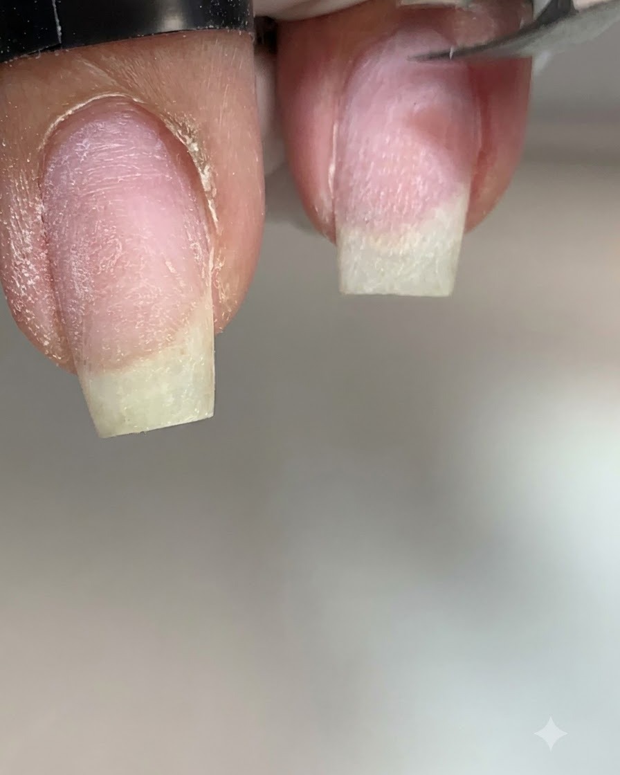 Un primer plano extremo de alicates de cutícula de metal recortando con precisión piel seca y levantada a lo largo del lateral izquierdo de una uña natural sin pintar.
