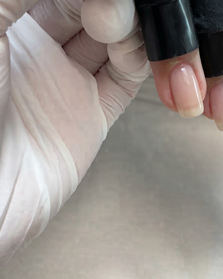 Un pincel de botella aplicando un gel rosa nude translúcido por el centro de una uña.