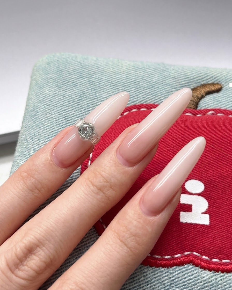 Primer plano de un pincel aplicando pigmento de gel blanco en la punta de una uña nude tipo stiletto.