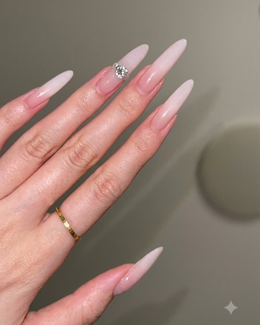 Un técnico de uñas usando un pincel con suaves golpecitos para crear un degradado blanco lechoso sobre una base nude.