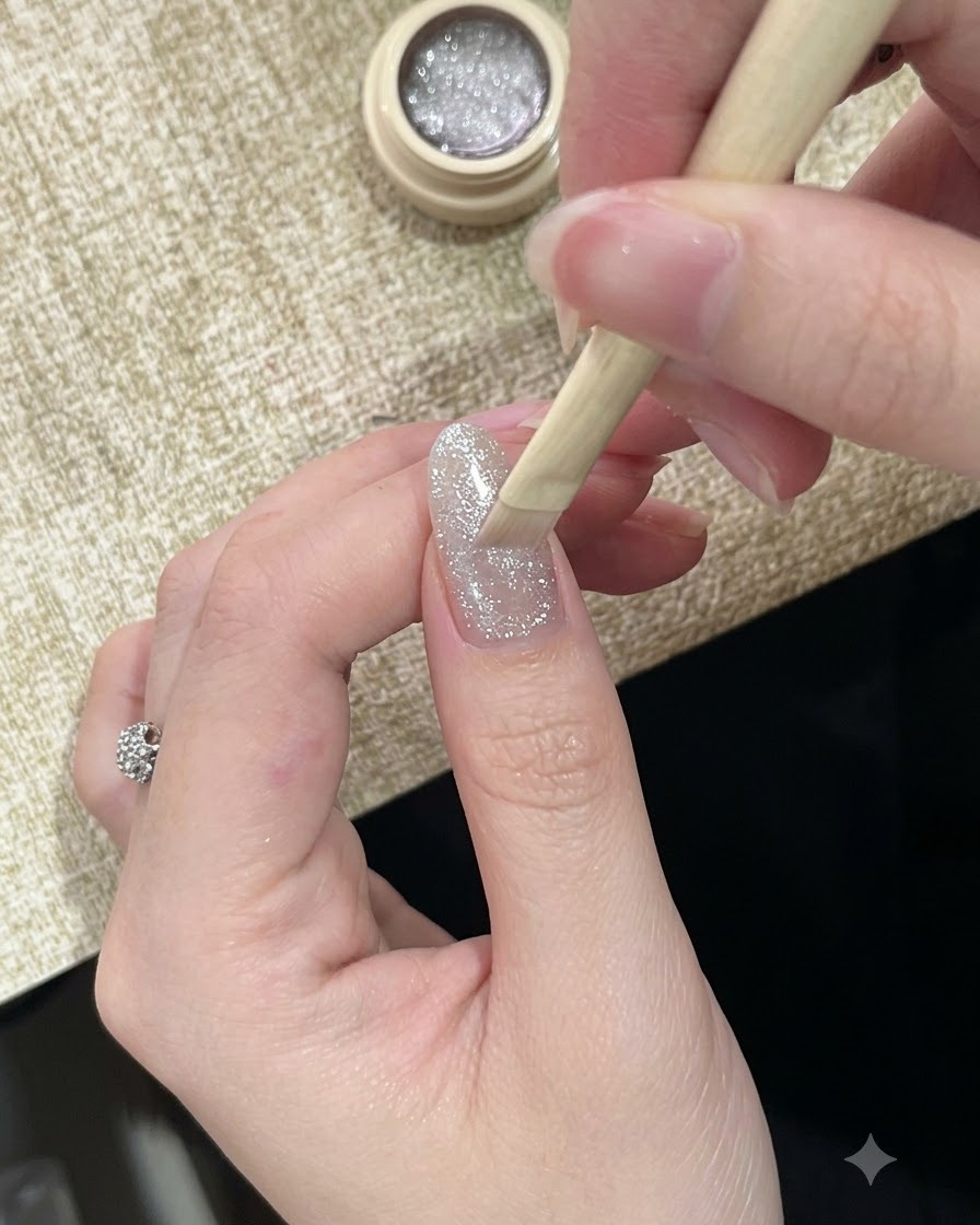 Un pincel aplicando un esmalte en gel ojo de gato plateado muy reflectante y brillante sobre una uña.