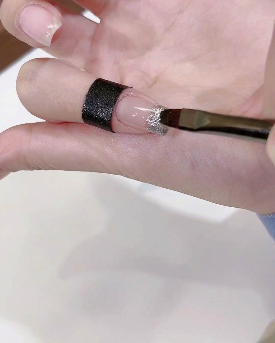 Un pincel aplicando un toque de pegamento de diamantes transparente sobre una uña decorada.