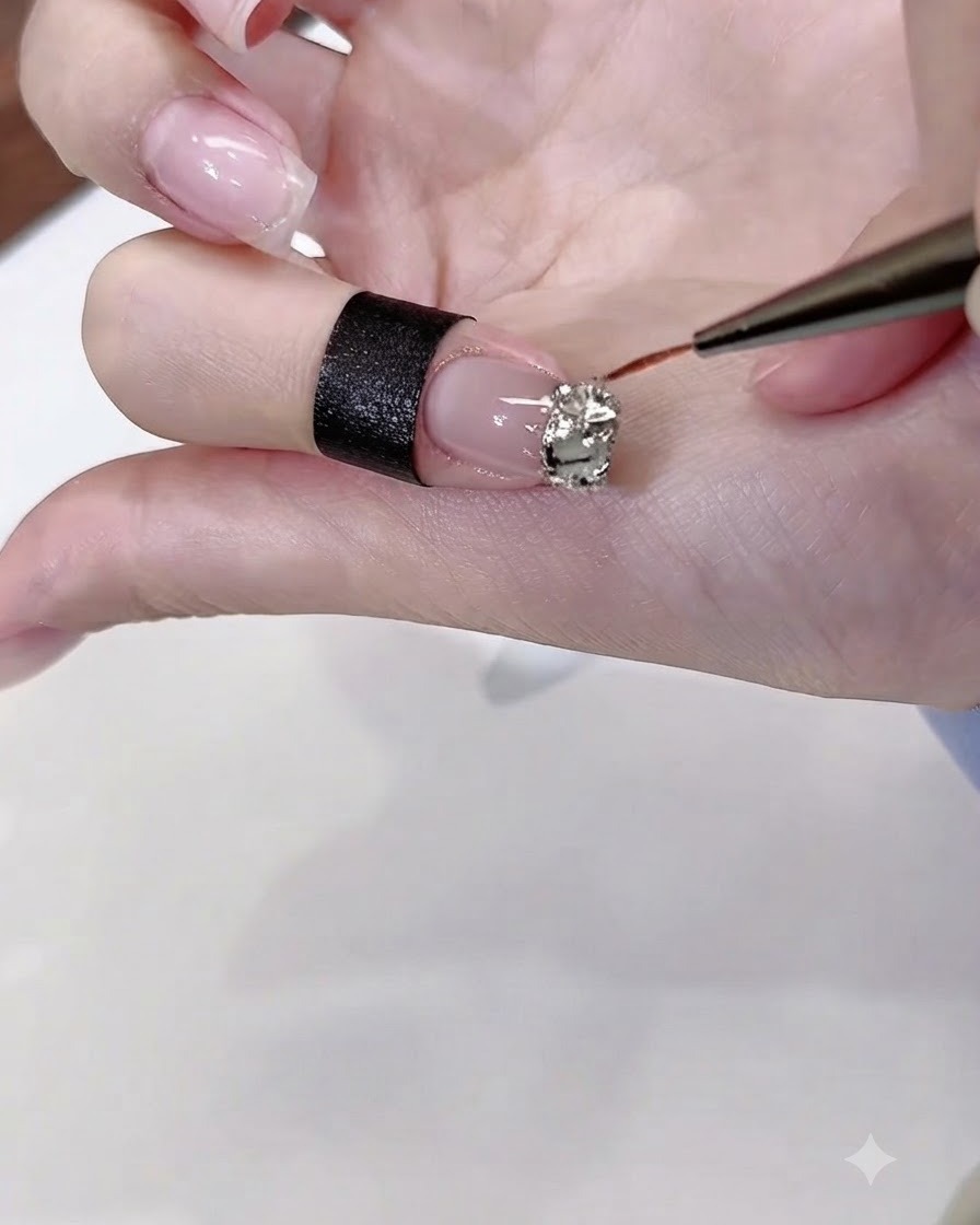 Un pincel fino para nail art aplicando pegamento de diamantes en gel transparente precisamente alrededor de los bordes de un grupo de pedrería en una uña pintada.