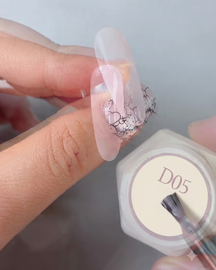 Pincel de manicura aplicando un top coat liso y brillante final sobre un diseño de uñas completo junto a un bote de gel etiquetado D05.