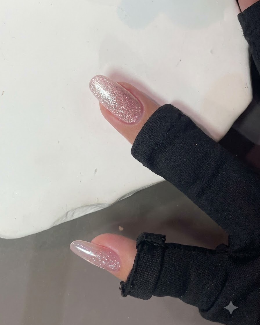 Un imán de uñas fuerte sostenido cerca de una uña brillante de purpurina rosa para formar un efecto de luz de ojo de gato.