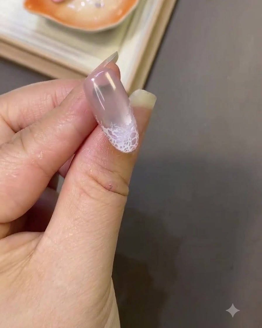 Primer plano de una uña mostrando un diseño de encaje blanco cerca de la punta con una textura de superficie lisa.