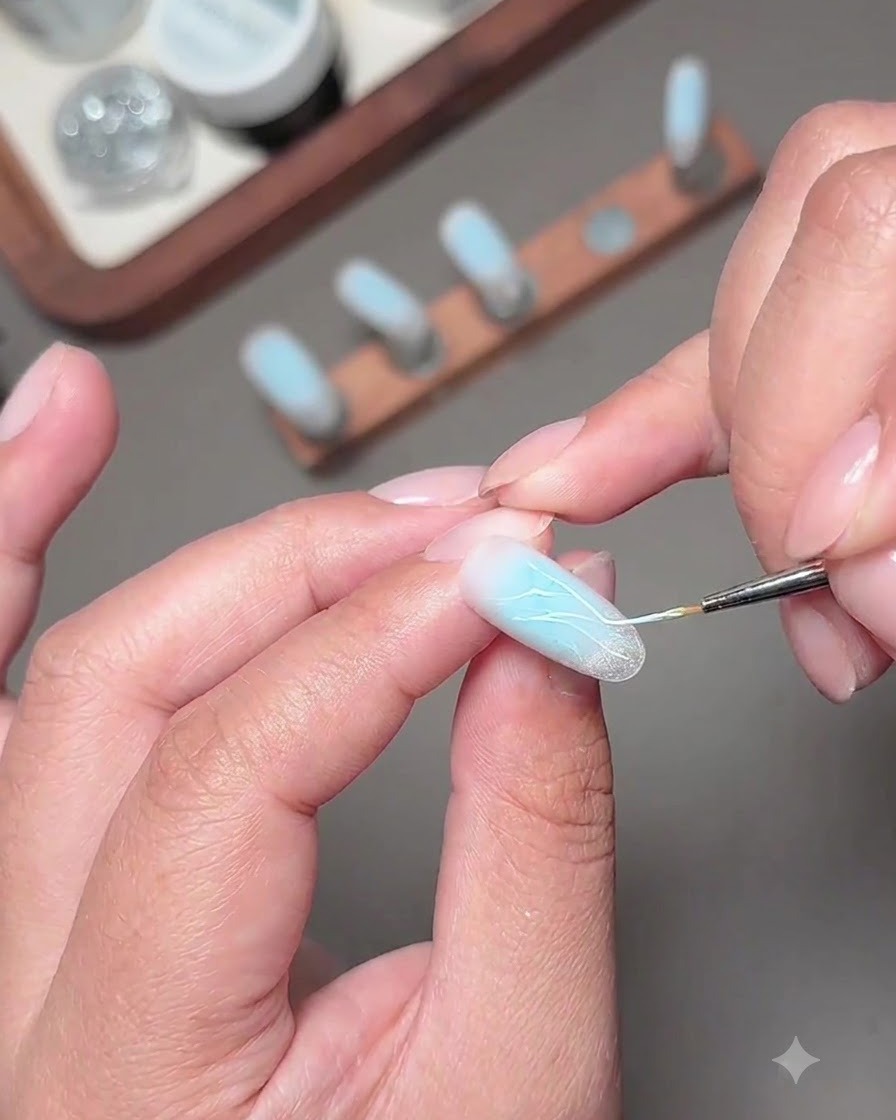 Un pincel fino aplicando líneas brillantes de gel de diamante fragmentado en la uña decorada.