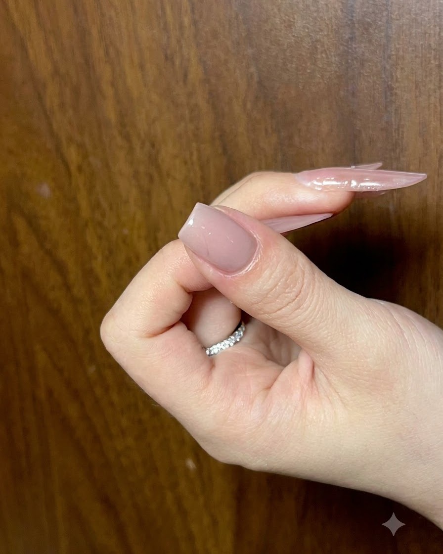 Una mano sosteniendo una uña con una capa base nude terminada, vista desde un ángulo para verificar la suavidad.