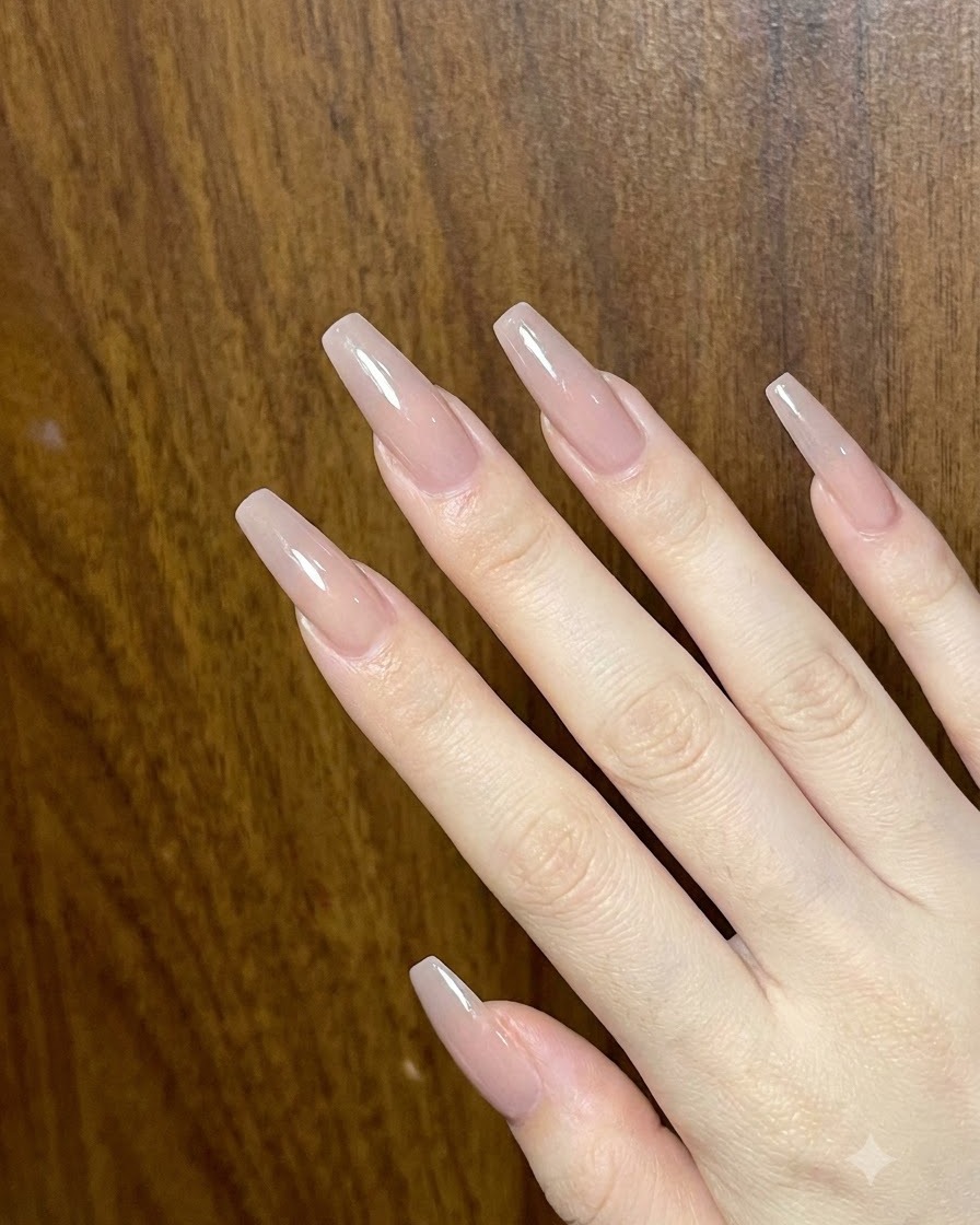 Una vista general de una mano que muestra múltiples uñas acrílicas largas y brillantes en tonos nude.