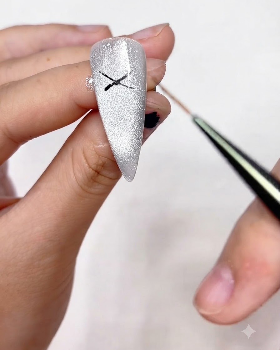 Un pincel delineador fino conectando las puntas de la forma de X dibujada previamente para crear los bucles del contorno de un lazo en una uña brillante.
